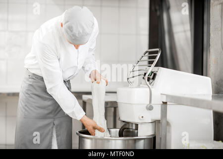 L'uomo mescolare l'impasto con impastatrice professionale macchina a livello di fabbricazione Foto Stock