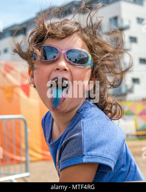 Cheeky giovane ragazza prendendo la sua linguetta blu colorata da un ghiaccio per lecca-lecca Foto Stock