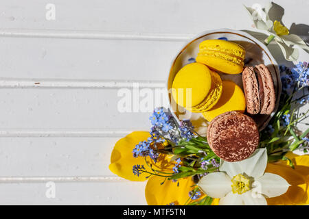 Fiori, macarons in colori pastello in bianco sullo sfondo di legno, vista dall'alto. Spazio di copia.amaretto al cioccolato e limone dessert isolato. Foto Stock
