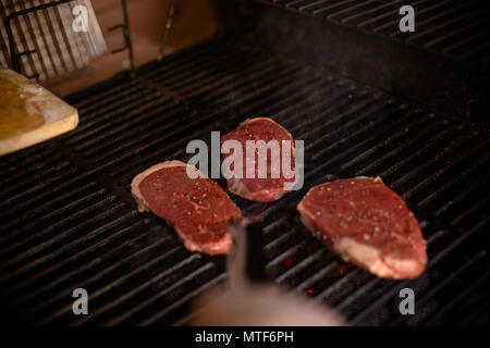 Mano di giovani uomini per grigliare carne alcuni .spiedini di carne su un enorme grill a gas.Vista dall'alto di crudo fresco carne alla griglia . Barbecue, grill e il concetto di cibo.grigliate di carne di manzo e di maiale Foto Stock