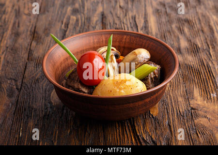 Stufato di carne con verdure in un tegame di coccio. funghi, carote, pomodori, sedano, cipolla. orizzontale Foto Stock