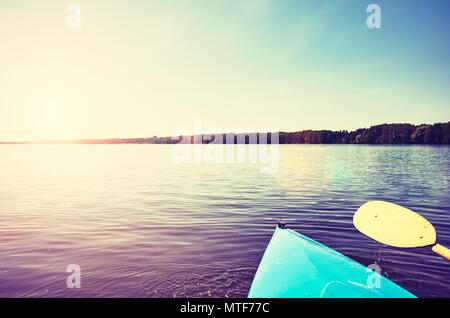 Prua di un kayak con paddle su un lago ancora al tramonto, dai toni di colore foto, messa a fuoco selettiva. Foto Stock