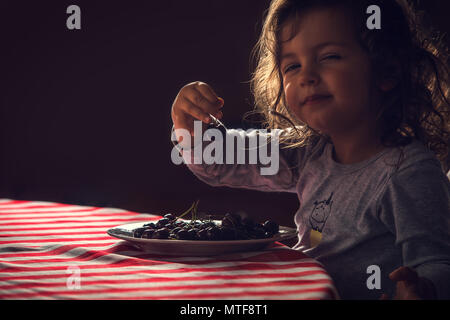 Carino bambina di mangiare le ciliegie per la sua prima colazione al mattino. Foto Stock