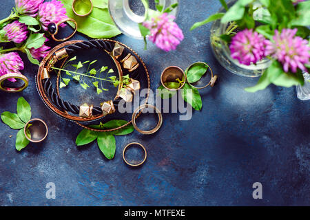 Golden bracciali e anelli in uno stile femminile concetto con fiori di trifoglio su uno sfondo scuro. Bella estate accessori. Foto Stock