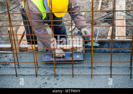 Builder utilizzando cazzuola di finitura per livellamento e buon calcestruzzo bagnato. Basamento in cemento pour con tondino e cassero. Foto Stock