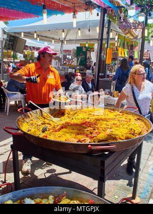 Madrid, Spagna - 15 maggio 2018. Un cuoco che serve la paella spagnola in una fase di stallo in una fiera gastronomica sotto l'occhio vigile di un ragazzo asiatico. Foto Stock