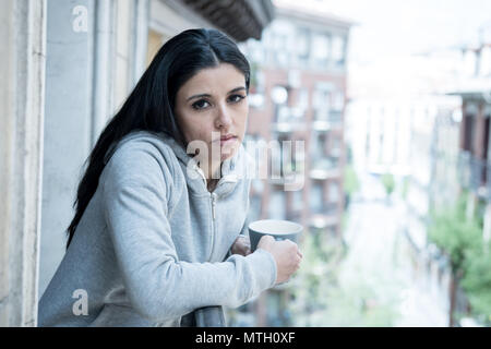 Bella donna latina affetti da depressione tenendo una tazza di caffè su un balcone a casa. Guardare fuori sensazione triste, il dolore e il lutto. Crisi, premere Foto Stock