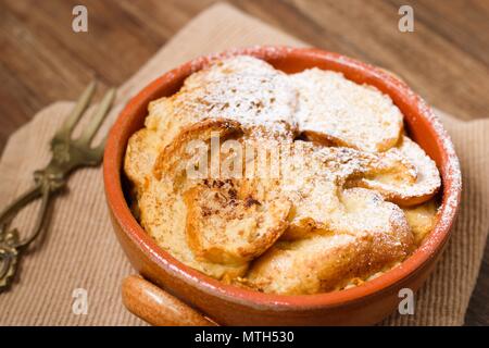 Pentola di coccio di il budino di pane e burro parzialmente coperto da zucchero a velo Foto Stock