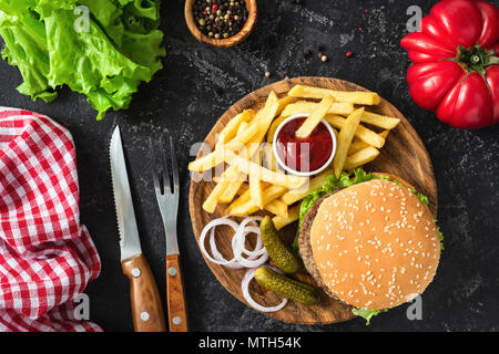 Hamburger di manzo con lattuga e pomodoro, patate fritte e ketchup su sfondo scuro. Tabella vista dall'alto. Il fast food, malsano concetto di mangiare Foto Stock