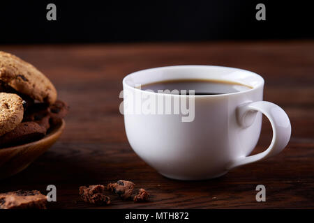 Caffè del mattino in porcellana bianca cup, croccante di scaglie di cioccolato cookie sul piatto piatto su un tavolo di legno, close-up, il fuoco selettivo, vista laterale. M in ceramica Foto Stock