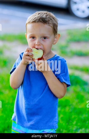 Ritratto di ragazzo con red succosa mela in mano e l'erba verde in background Foto Stock