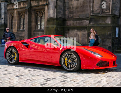 Le persone guardano enviously ad un luminoso rosso Ferrari 488 GTB coupe Auto sportiva, parcheggiato sulla strada di ciottoli, Royal Mile di Edimburgo, Scozia, Regno Unito Foto Stock