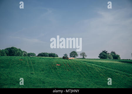 Maggio 29, 2018, Cork, Irlanda - un trattore che solcano l'erba del campo in una giornata di sole Foto Stock