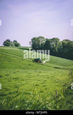 Maggio 29, 2018, Cork, Irlanda - un trattore che solcano l'erba del campo in una giornata di sole Foto Stock