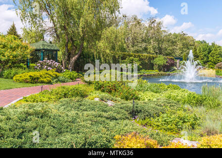 Frammento del parco in Mezhigiri vicino a Kiev. Una piccola fontana sul lago. La boccola di fioritura dei rododendri, un frammento del lago e un beauti Foto Stock