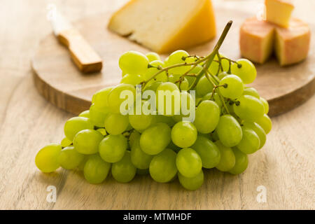 Fresca uva verde con sullo sfondo il formaggio su una tavola di legno Foto Stock