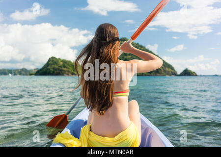 Vista posteriore di una giovane donna paddling con un doppio-bladed pagaiare in canoa sul mare durante le vacanze estive in sull isola di Flores, Indonesia Foto Stock