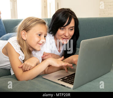 Bella bionda carino bambina e la mamma a giocare insieme sorridente e avente il tempo di incollaggio utilizzando un computer portatile sul divano di casa. La famiglia felice, digitale Foto Stock