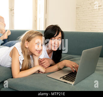 Bella bionda carino bambina e la mamma a giocare insieme sorridente e avente il tempo di incollaggio utilizzando un computer portatile sul divano di casa. La famiglia felice, digitale Foto Stock