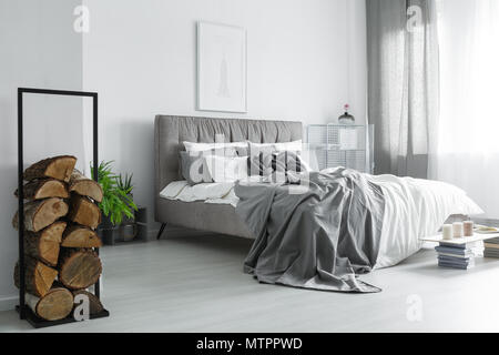 Accogliente camera da letto con pezzi di legna da ardere impilati in nero telaio metallico Foto Stock