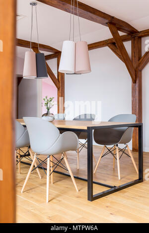 Progettato lampade al di sopra di un tavolo da pranzo con sedie grigio in camera spaziosa con una costruzione in legno Foto Stock