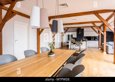 Le lampade moderne sopra lungo tavolo da pranzo in legno con vaso decorativo e sedie grigio in ampio loft Foto Stock