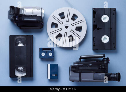 Videocamere VHS e Mini cassette e un rotolo di pellicola ben disposti su sfondo blu, sopra visualizza Foto Stock