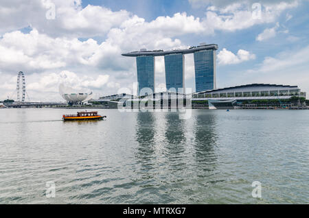 Una barca di crociera noto come twakows ride passa la famosa Marina Bay Sands Hotel. La barca sono stati utilizzati per scopi di trasporto lungo il Fiume Singapore. Foto Stock