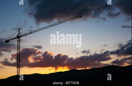 Costruzione di gru su silhouette tramonto rosso e colline. Stato reale sul concetto di campagna Foto Stock