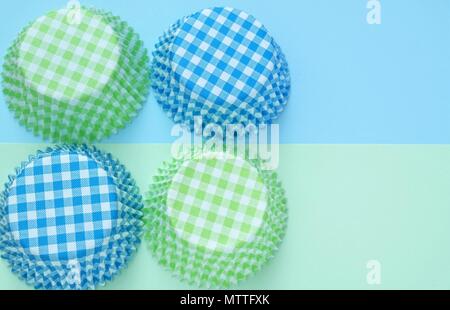 Quattro cupcake stampi di carta, disposti in quadrato. sfondo di cottura in blu e verde pastello. vista superiore e lo spazio di testo. Foto Stock