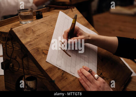 Vista sul grande foglio di carta bianca tela con parola calligrafia scritto sulla parte superiore utilizzando la spazzola con inchiostro nero dal progettista del font o artista creativa freelancer Foto Stock