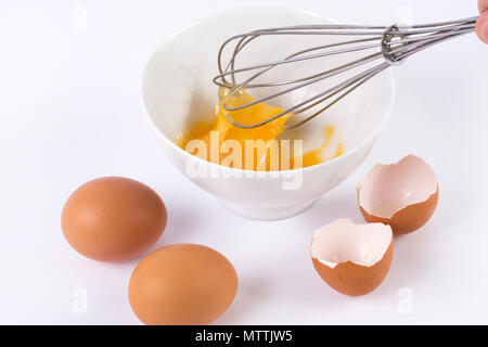 L'uomo sbattere le uova. Uova di panna montata in bianco ciotola con due e rotture di vuoto guscio d'uovo su sfondo bianco. Il cibo e il concetto di cucina a vista Foto Stock