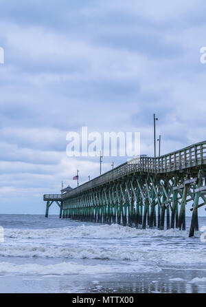 Sotto il molo - Splendide vedute dell'oceano da Oak Island Beach, onde che si infrangono e il molo in legno in un giorno nuvoloso. Foto Stock