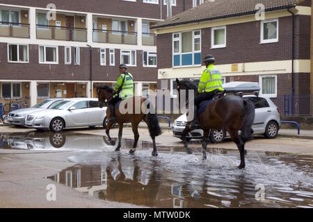 Due poliziotti Metropolitano di cavalli che sono trotto attraverso una pozzanghera sulla strada per il maneggio in prua, Tower Hamlets, Londra Foto Stock