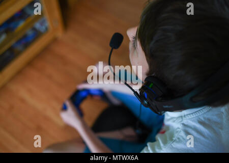 Un giovane ragazzo con una testa di gioco impostato e microfono sulla riproduzione su una playstation. Foto Stock