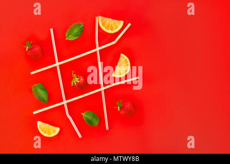 Tic Tac Toe gioco fatto di cannucce cocktail, fragola, menta e le fette di limone in bright sfondo rosso con copia spazio. La limonata, bibite estive. Il minimo Foto Stock