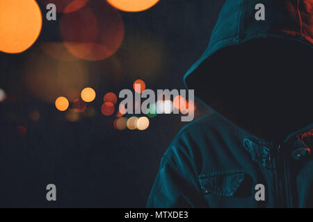 Volto hooligan con hoodie in ambiente urbano circostante, chiave di basso ritratto del cappuccio maschio a persona per le strade delle città di notte Foto Stock