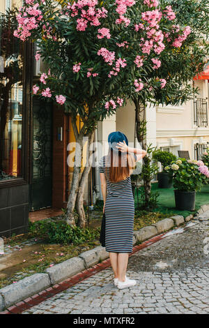 Una giovane ragazza in un cappello ammira i bellissimi fiori accanto alla casa Foto Stock