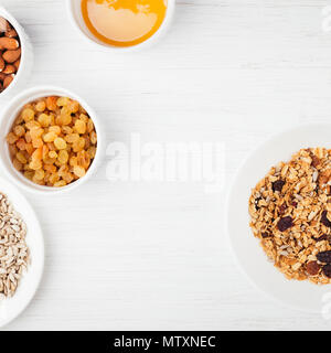 Sana colazione con muesli. Il campo di bocce di granola e gli ingredienti sul bianco tavolo in legno. Vista da sopra con posto per il testo. Foto Stock