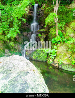 Silky cascata che scorre attraverso la vegetazione verde e su moss ricoperta di rocce. Foto Stock