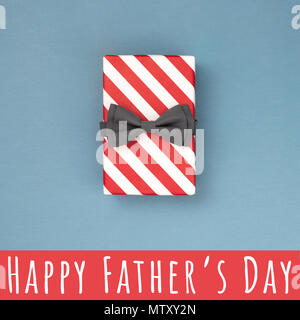 Una scatola regalo fasciata in rosso a strisce di carta e legato con il grigio bow tie su blu-grigio. Festa del papà card concept. Foto Stock