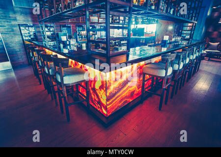 Il bar contemporaneo contatore con le attrezzature e le comode sedie per bar nel ristorante moderno. Elegante arredamento interno. Il blu scuro e il colore rosso combinazione. Foto Stock