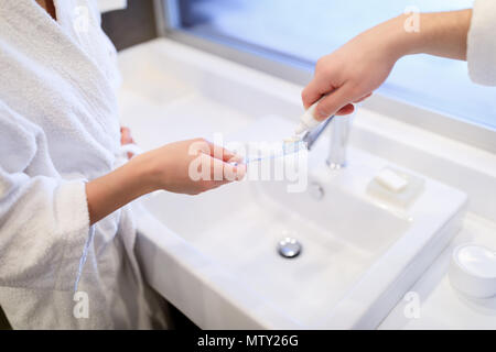 Immagine ritagliata del fidanzato applicando una pasta dentifricia sulla ragazza spazzolino da denti nella stanza da bagno Foto Stock