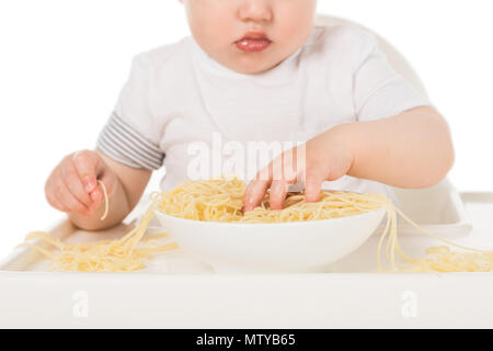 Ritagliato colpo di baby boy mangiare spaghetti con le mani e la seduta nel seggiolone Foto Stock