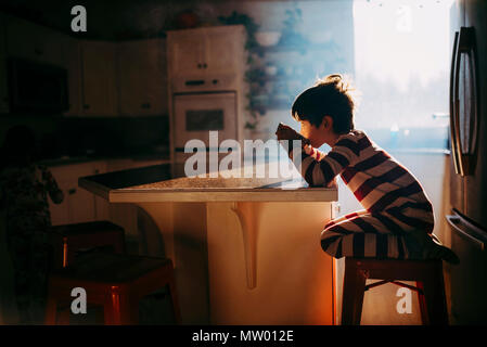 Ragazzo seduto in cucina a mangiare la sua colazione nella luce del mattino Foto Stock