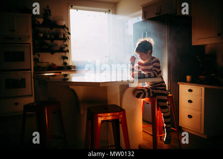 Ragazzo seduto in cucina a mangiare la sua colazione nella luce del mattino Foto Stock