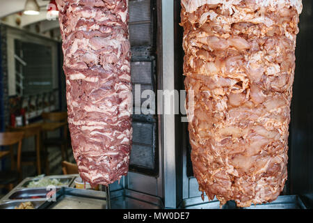 Alimenti crudi per outdoor shawarma - due tipi di carne sul grill verticale su cucina sfondo con verdure in contenitori di acciaio inox. Foto Stock