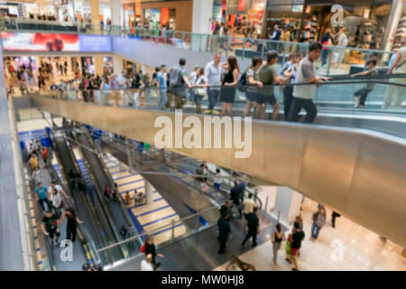 Le persone andare a fare shopping all'interno del centro commerciale. Gli spazi con i vari negozi sono sviluppate su diversi piani collegati da lunghe scale mobili. sfocato Foto Stock