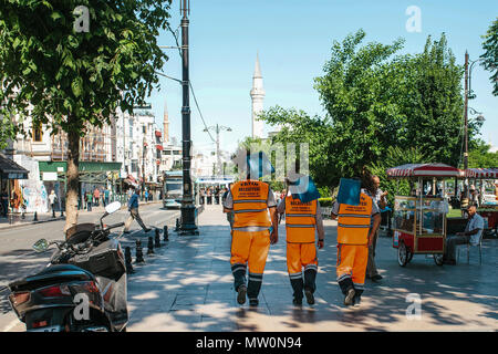 Immagine editoriale di tre street portieri in arancio brillante uniformi sono a piedi giù per la strada tenendo scope e tegami di polvere. Foto Stock