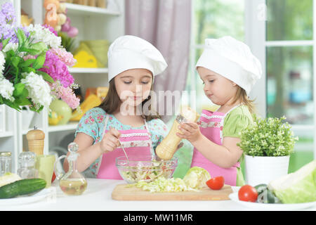 Due adorabili bambine in grembiuli preparare deliziose insalate Foto Stock